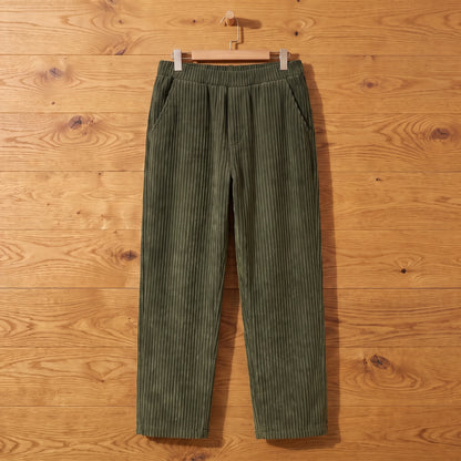 Green thick rib corduroy trousers hanging on an oak wall