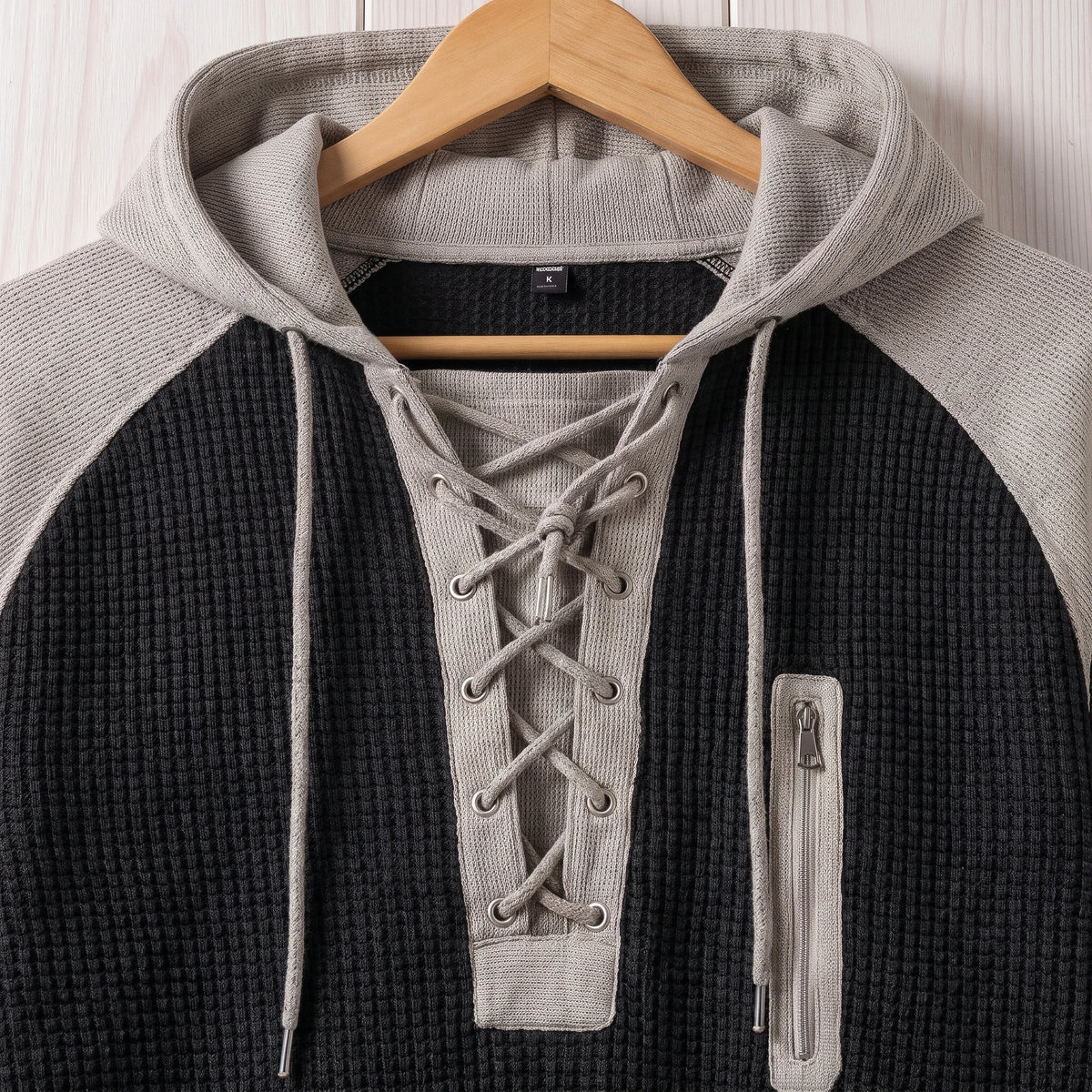 Close-up of the lace-up neck and zip chest pocket on the black waffle knit hooded sweater