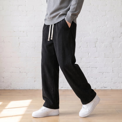 Man walking in the black wide corduroy trousers with a grey sweater and white sneakers