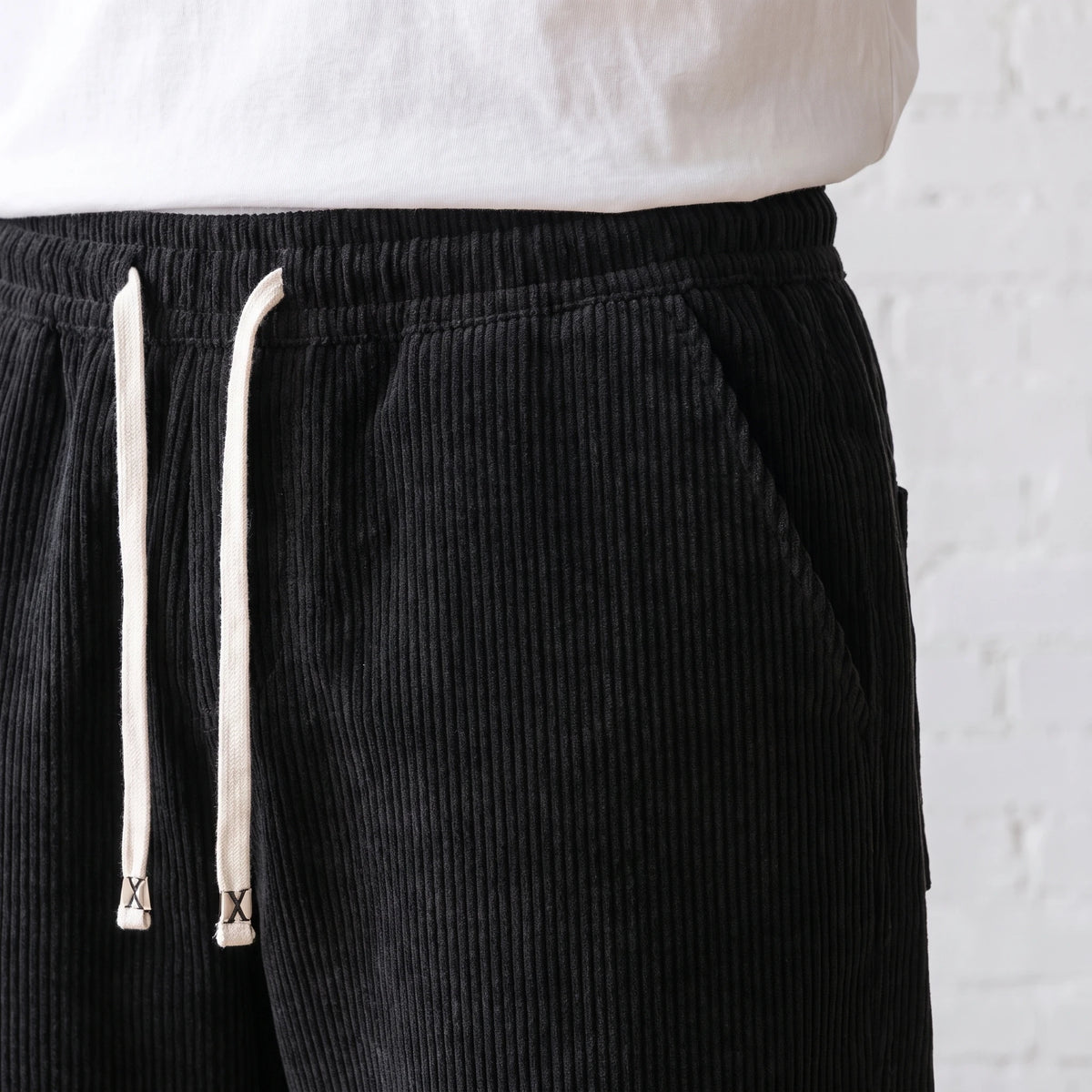 Close-up of the elastic waistband, white drawstring and side pocket on the black corduroy trousers