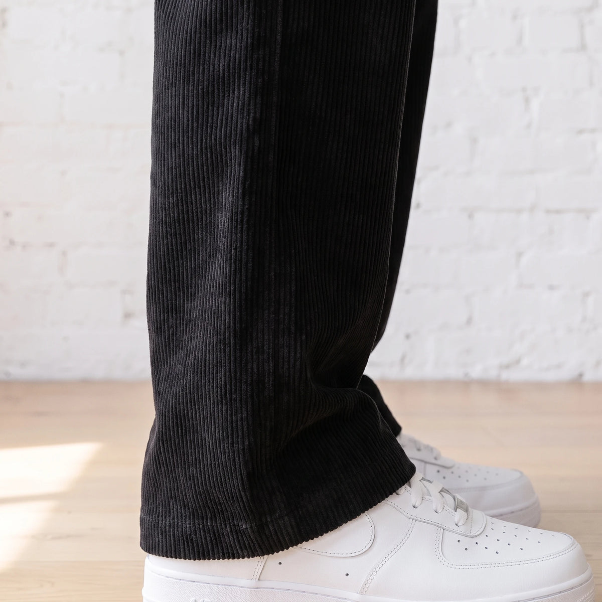 Close-up of the wide corduroy ribs on the lower leg of the black trousers