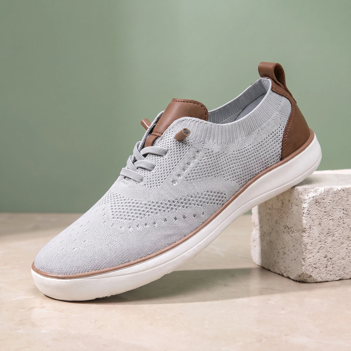 Grey knit lace-up shoe with a white sole on a limestone block